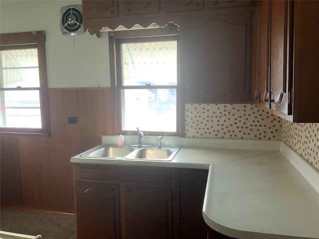 kitchen featuring dark brown cabinetry, plenty of natural light, wooden walls, and sink