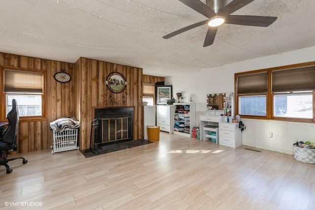 interior space with a textured ceiling, ceiling fan, light hardwood / wood-style flooring, and wooden walls