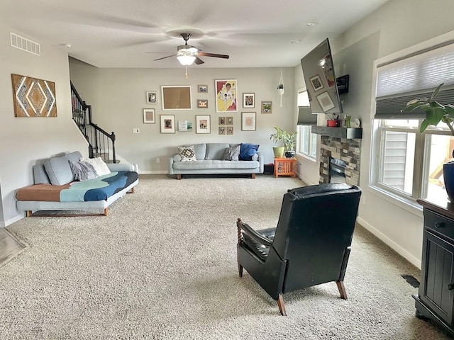 carpeted living room with a stone fireplace and ceiling fan