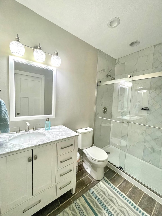 bathroom with a textured ceiling, vanity, toilet, and walk in shower