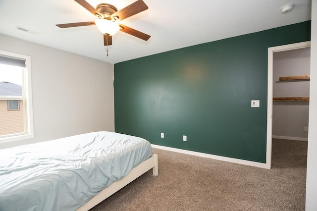 carpeted bedroom with visible vents, baseboards, ceiling fan, and a walk in closet