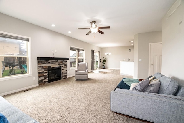 living room with carpet, ceiling fan with notable chandelier, a stone fireplace, and visible vents
