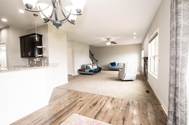 unfurnished living room featuring visible vents, light wood-type flooring, stairs, ceiling fan with notable chandelier, and recessed lighting