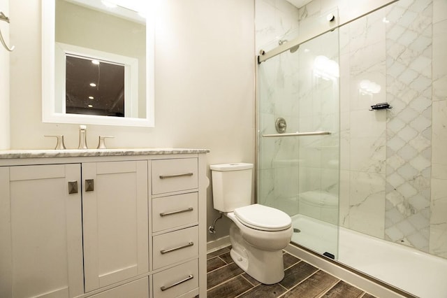 bathroom with wood tiled floor, baseboards, vanity, toilet, and a marble finish shower