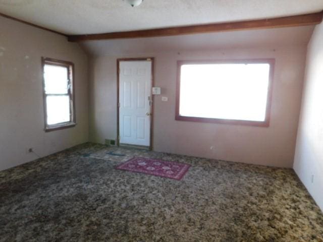 foyer entrance with lofted ceiling with beams, carpet, and a healthy amount of sunlight