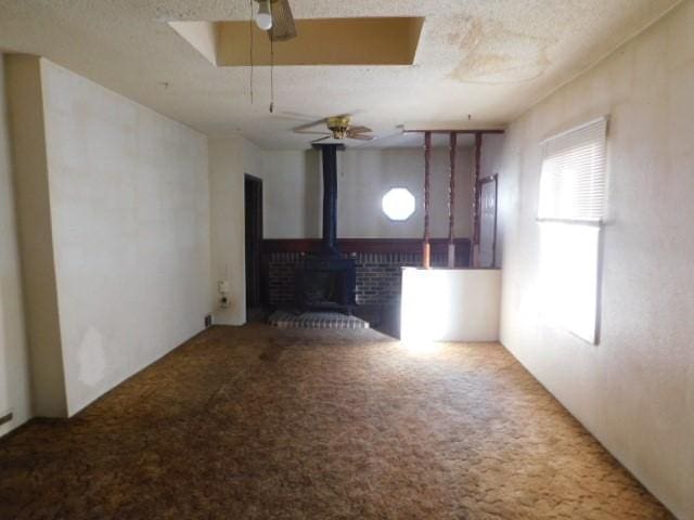 unfurnished living room with a textured ceiling, ceiling fan, a wood stove, and carpet floors