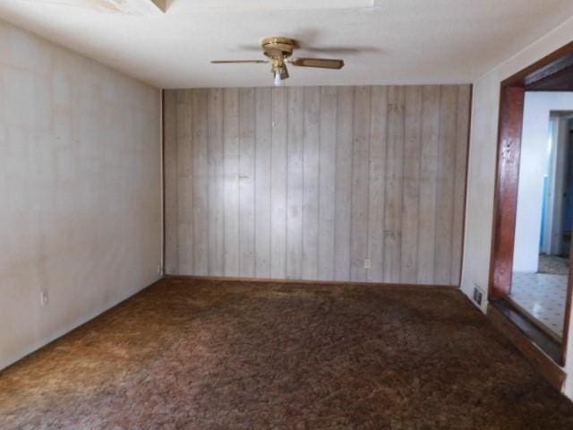 unfurnished room featuring carpet flooring, ceiling fan, and wood walls