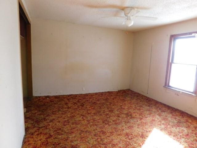 carpeted empty room featuring ceiling fan and a textured ceiling