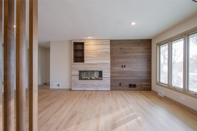 unfurnished living room featuring wooden walls, a tile fireplace, and light hardwood / wood-style flooring