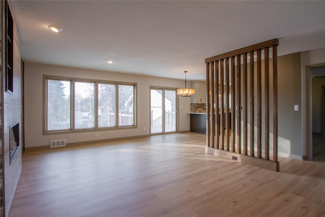 unfurnished living room with a large fireplace, an inviting chandelier, and light hardwood / wood-style flooring