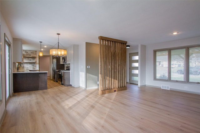 unfurnished living room featuring light hardwood / wood-style floors, sink, and a chandelier