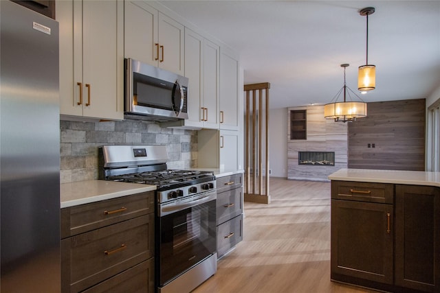 kitchen featuring hanging light fixtures, stainless steel appliances, tasteful backsplash, white cabinets, and light wood-type flooring