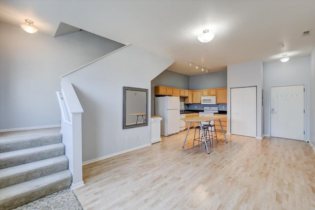 kitchen with a center island, white appliances, light wood-type flooring, a breakfast bar area, and light brown cabinetry