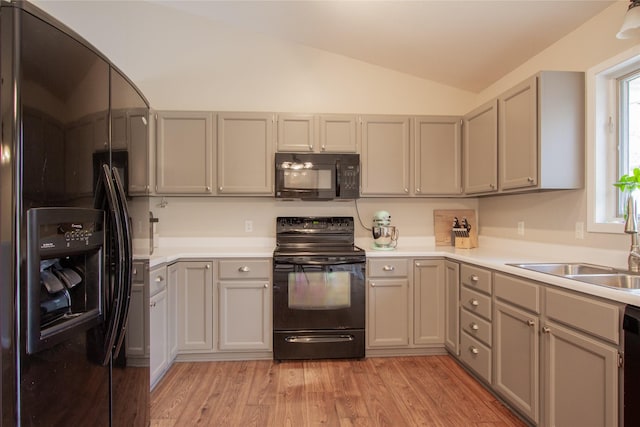 kitchen with gray cabinetry, lofted ceiling, black appliances, sink, and light hardwood / wood-style floors