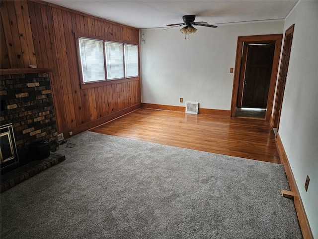 unfurnished living room featuring ceiling fan, hardwood / wood-style flooring, wooden walls, a fireplace, and ornamental molding