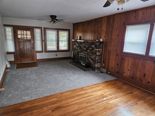 unfurnished living room with hardwood / wood-style floors, ceiling fan, wood walls, and a brick fireplace