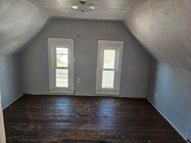 additional living space featuring vaulted ceiling, dark wood-type flooring, and a textured ceiling