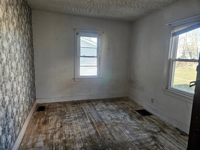 empty room with dark wood-type flooring, a healthy amount of sunlight, and a textured ceiling