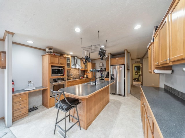 kitchen featuring pendant lighting, a center island with sink, wall chimney exhaust hood, a kitchen bar, and stainless steel appliances