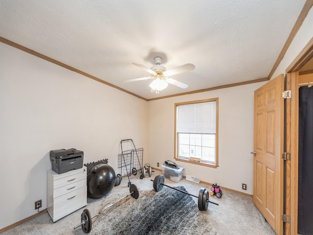 workout area with ceiling fan, crown molding, light colored carpet, and a textured ceiling