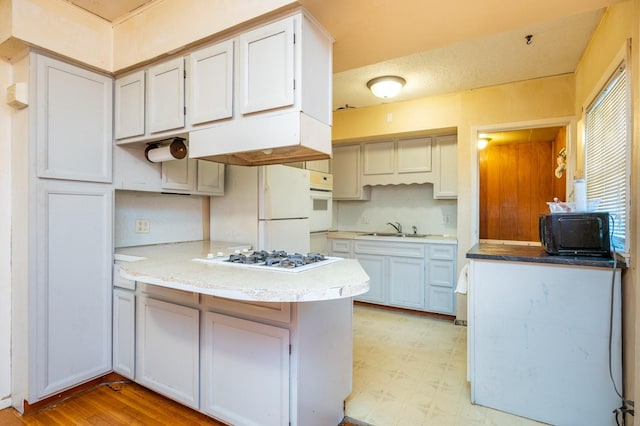 kitchen with white appliances, sink, kitchen peninsula, light hardwood / wood-style flooring, and white cabinetry