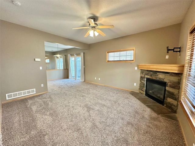 unfurnished living room with a stone fireplace, ceiling fan, carpet floors, and a textured ceiling