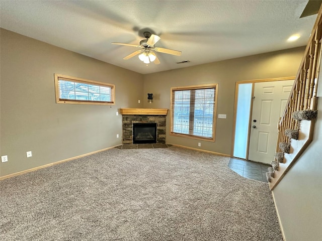 unfurnished living room featuring a stone fireplace, ceiling fan, carpet, and a textured ceiling