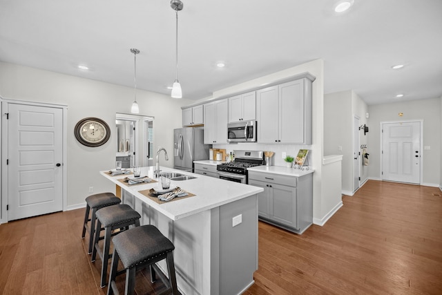 kitchen with a kitchen bar, appliances with stainless steel finishes, sink, decorative light fixtures, and a center island with sink