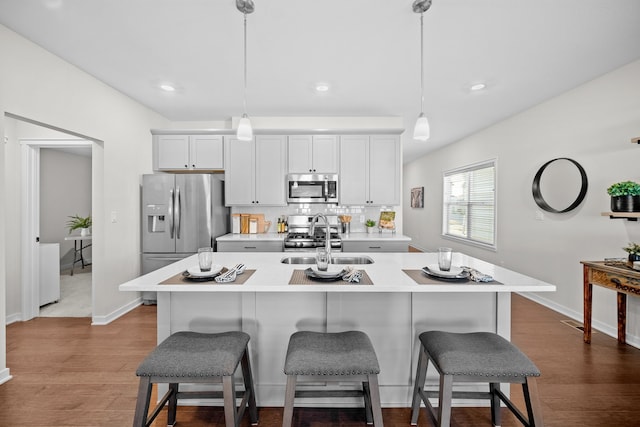 kitchen with sink, an island with sink, decorative light fixtures, white cabinets, and appliances with stainless steel finishes