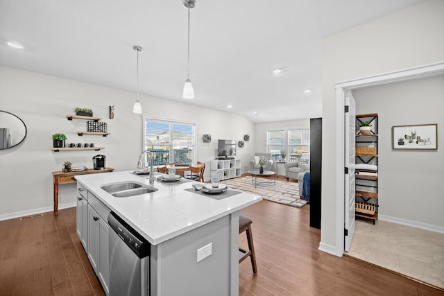 kitchen with sink, stainless steel dishwasher, dark hardwood / wood-style floors, an island with sink, and pendant lighting