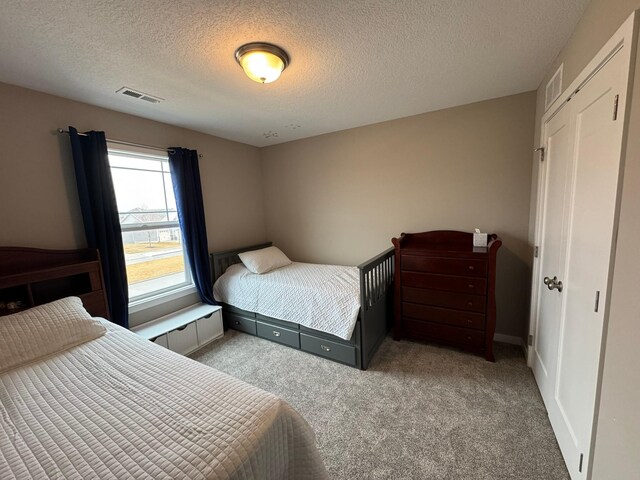 bedroom with visible vents, a textured ceiling, and carpet flooring