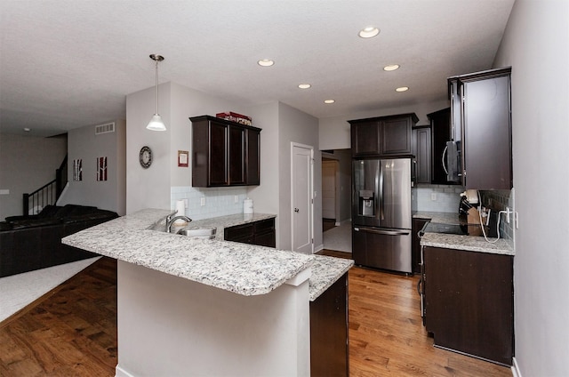 kitchen with light wood finished floors, stainless steel fridge, dark brown cabinetry, a peninsula, and a sink