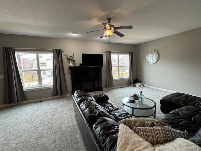 living room featuring light colored carpet, a ceiling fan, a glass covered fireplace, a textured ceiling, and baseboards