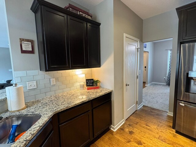 kitchen with tasteful backsplash, light stone countertops, light wood-type flooring, stainless steel fridge, and baseboards