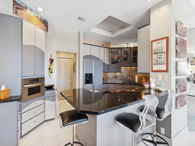 kitchen with tasteful backsplash, kitchen peninsula, a kitchen bar, light tile patterned floors, and appliances with stainless steel finishes