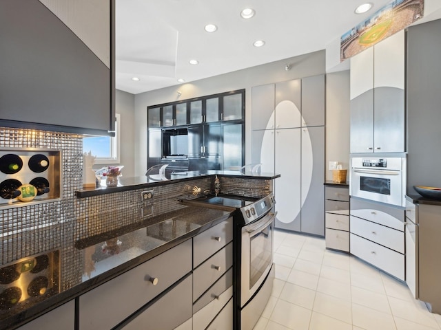 kitchen featuring range with electric cooktop, wall oven, backsplash, dark stone counters, and light tile patterned floors