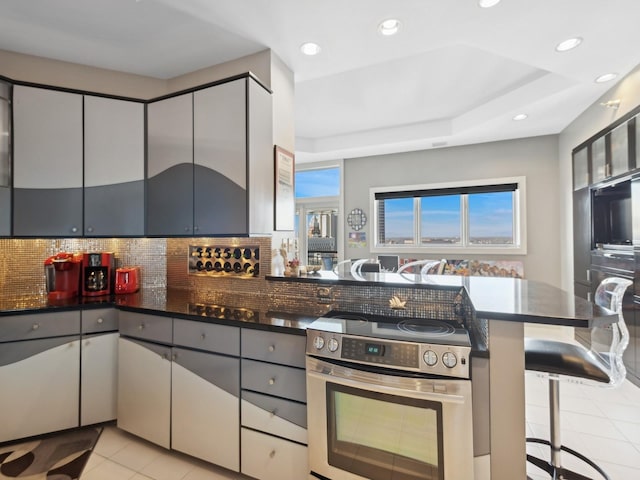 kitchen with kitchen peninsula, a kitchen breakfast bar, gray cabinetry, a raised ceiling, and electric range