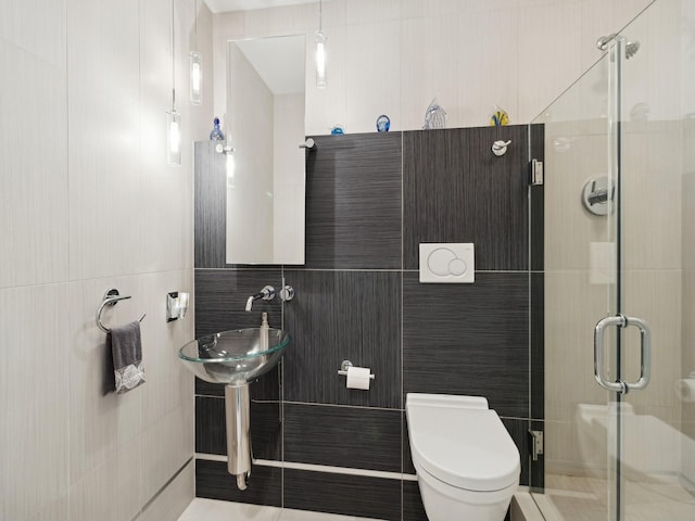 bathroom featuring toilet, a shower with shower door, and tile walls