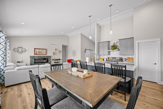 dining room with light wood-type flooring, high vaulted ceiling, a stone fireplace, and a barn door