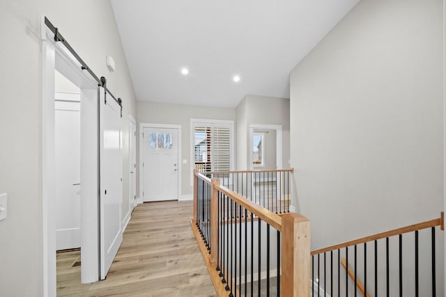 corridor featuring recessed lighting, a barn door, light wood-style floors, an upstairs landing, and baseboards