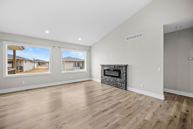 unfurnished living room featuring a wealth of natural light, lofted ceiling, visible vents, a stone fireplace, and wood finished floors