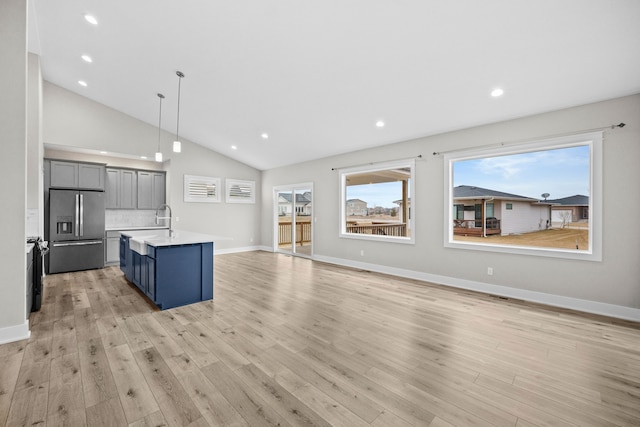 kitchen featuring decorative backsplash, stainless steel fridge with ice dispenser, light wood-style flooring, a kitchen island with sink, and light countertops