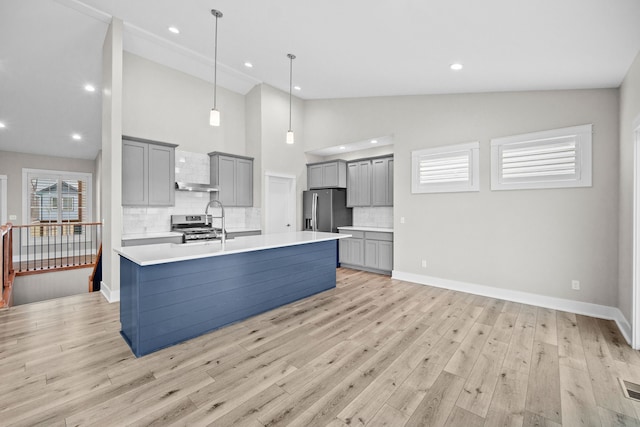 kitchen with gray cabinetry, light countertops, appliances with stainless steel finishes, light wood finished floors, and a center island with sink