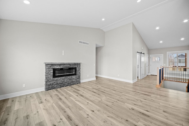 unfurnished living room with visible vents, a barn door, a stone fireplace, wood finished floors, and baseboards