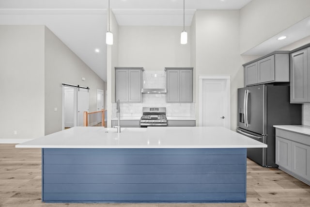 kitchen featuring stainless steel appliances, a barn door, gray cabinets, and a center island with sink