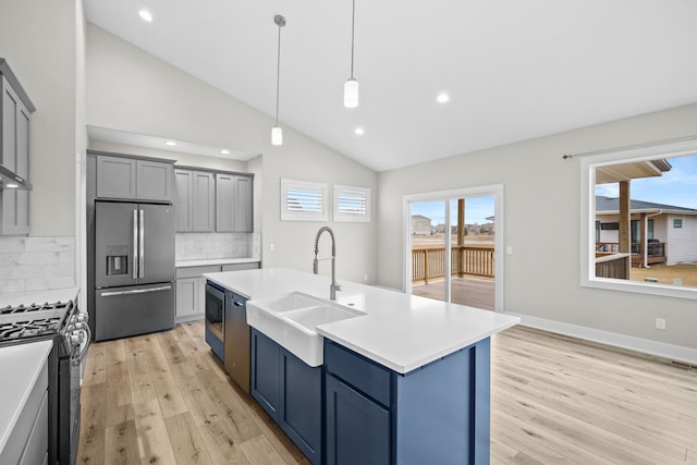 kitchen with a sink, light countertops, light wood-type flooring, range with gas cooktop, and stainless steel fridge