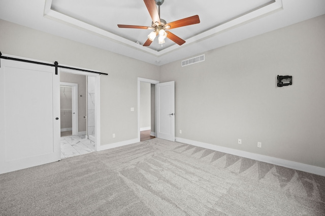 unfurnished bedroom with light colored carpet, a raised ceiling, visible vents, and a barn door