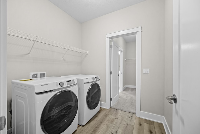 washroom featuring a textured ceiling, laundry area, baseboards, washer and dryer, and light wood finished floors