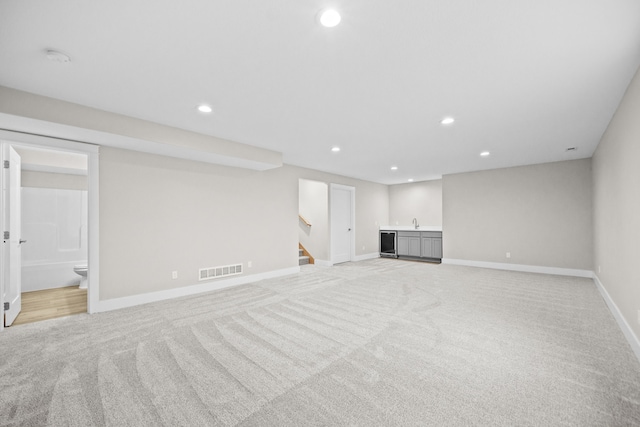 finished below grade area with visible vents, stairs, indoor wet bar, light carpet, and recessed lighting