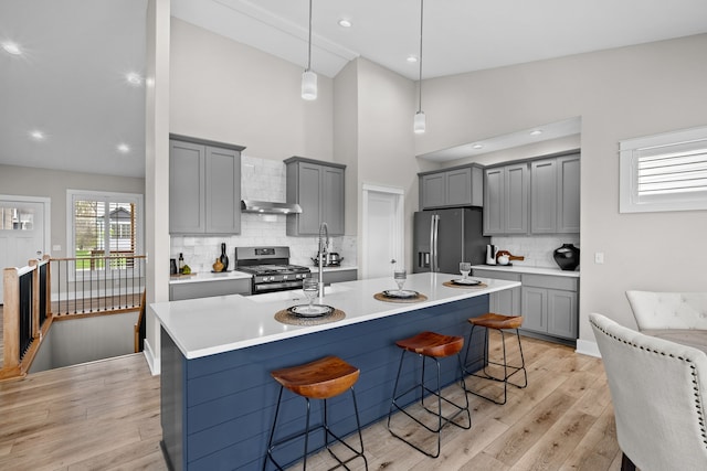 kitchen with decorative backsplash, a breakfast bar, gray cabinets, light wood-style flooring, and stainless steel appliances